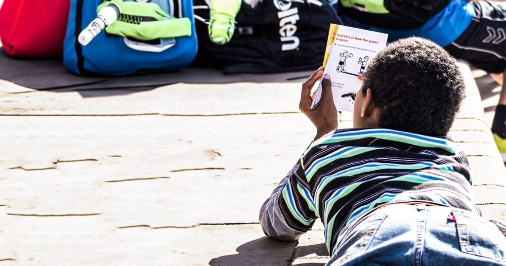 A little boy is lying on the floor, attentively reading a manual describing various sports exercises.