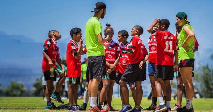 Ein freiwilliger Sporttrainer berät sich während eines Turniers mit den jungen Spieler seiner Mannschaft auf dem Spielfeld.