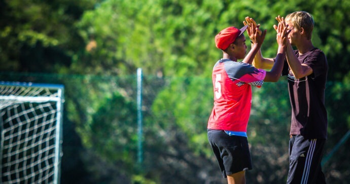 Ein freiwilliger Sporttrainer und ein junger Spieler geben sich auf dem Sportplatz ein "High Five".