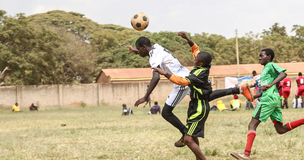 Football scene with three players from the Football for a Good project jumping for a header.