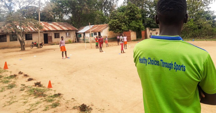 Der Projektbetreuer der HESPO steht am Rande eines sandigen Spielfeldes in seinem Dorf in Kenia und beobachtet die Handballspieler seiner Mannschaft.