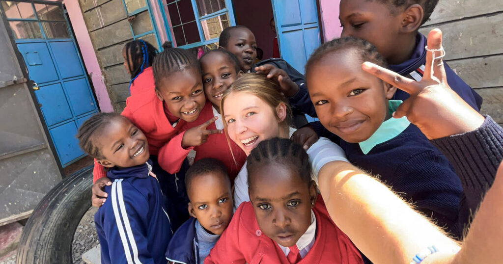 A volunteer sports coach takes a selfie surrounded by smiling children from her sports project.