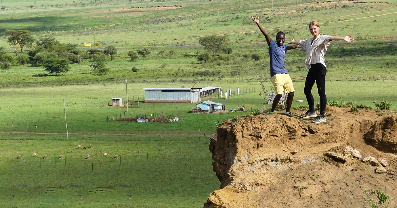 A sports volunteer poses with outstretched arms with a local man in a rural area of Kenya.