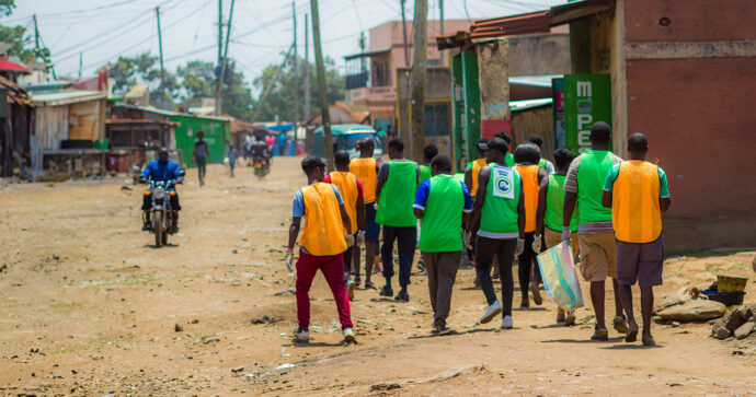 Eine Gruppe von Projektteilnehmern in bunten Sporttrikots sammelt Müll auf einer holprigen Straße in Kenia.